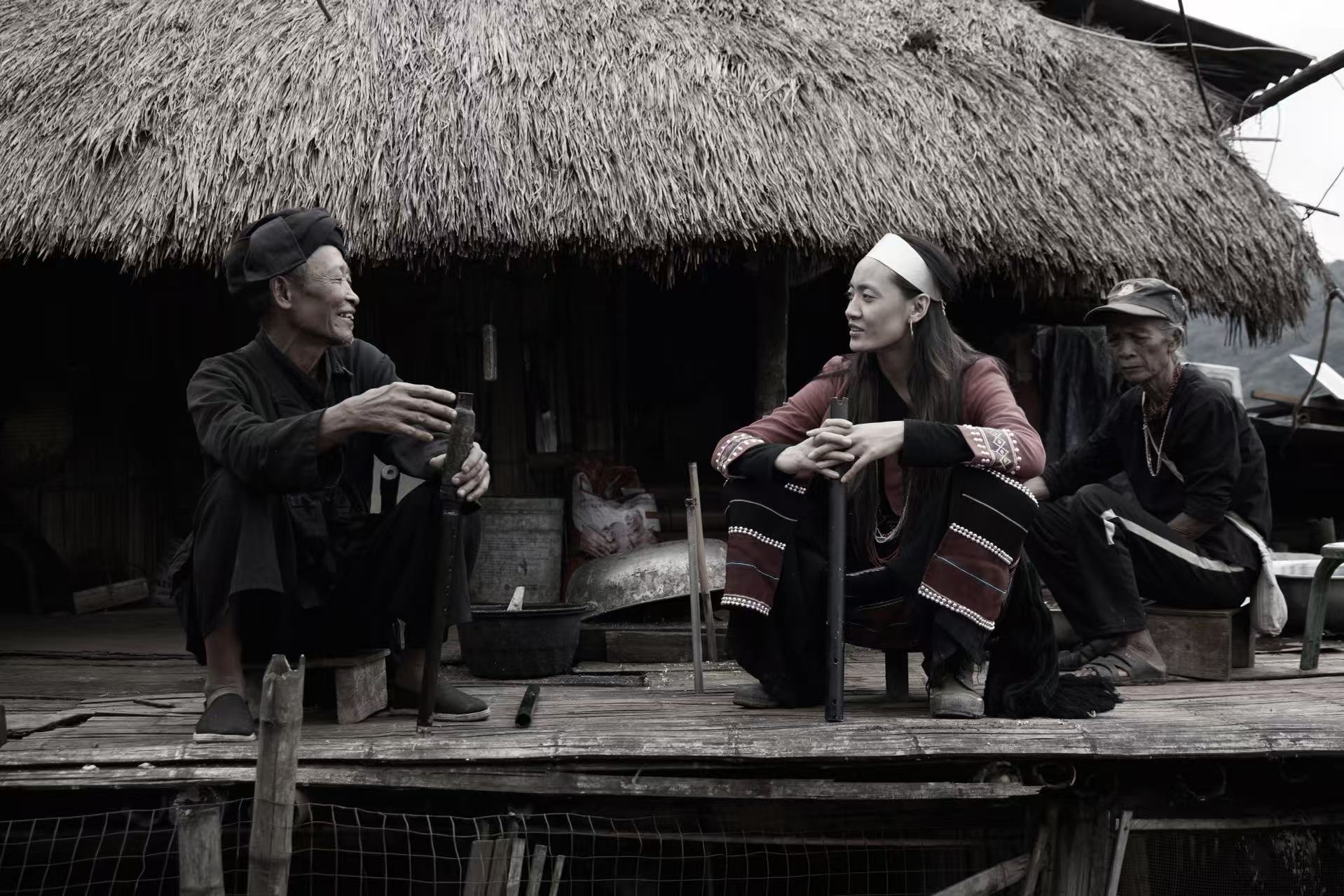 Dong Jilan talking with heritage practitioners in front of a thatched house